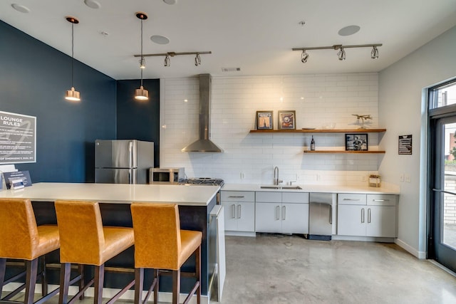 kitchen featuring sink, white cabinets, tasteful backsplash, wall chimney range hood, and appliances with stainless steel finishes