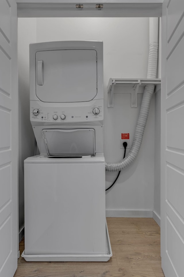 clothes washing area with stacked washer and clothes dryer and light wood-type flooring