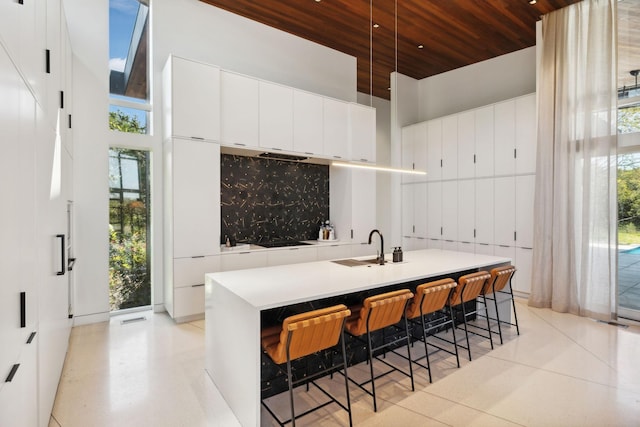 kitchen with a kitchen breakfast bar, white cabinets, wooden ceiling, a kitchen island with sink, and a high ceiling