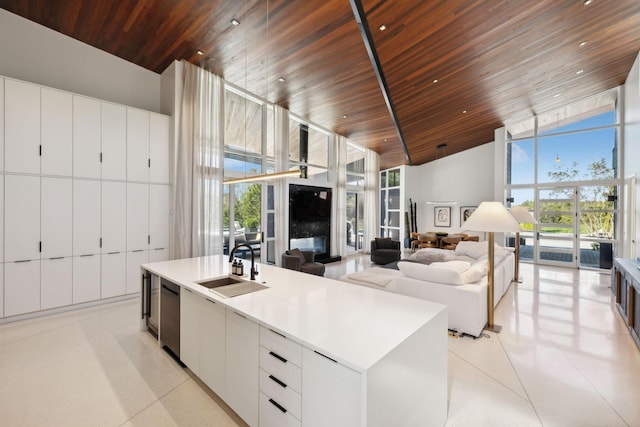 kitchen with a kitchen island with sink, wooden ceiling, a towering ceiling, sink, and white cabinetry