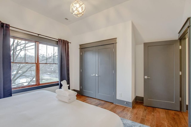 bedroom with a closet, vaulted ceiling, a notable chandelier, and light hardwood / wood-style flooring