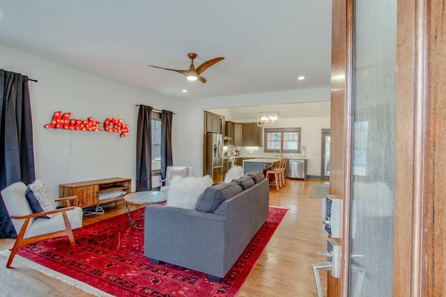 living room featuring ceiling fan with notable chandelier and light wood-type flooring