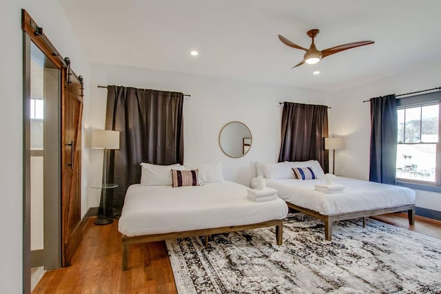 bedroom featuring ceiling fan, a barn door, and light hardwood / wood-style flooring