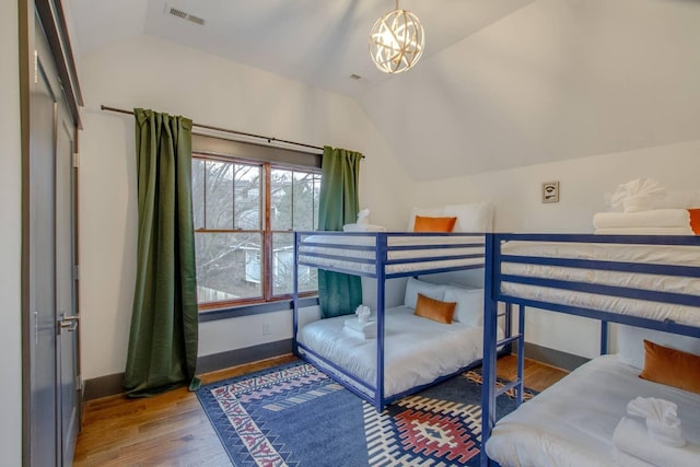 bedroom with lofted ceiling, an inviting chandelier, and hardwood / wood-style floors