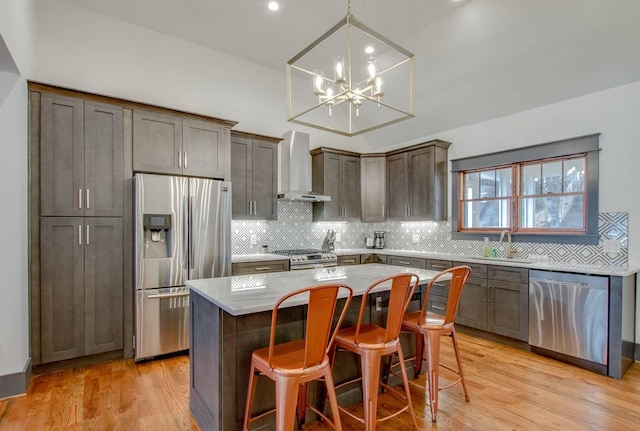 kitchen with appliances with stainless steel finishes, a breakfast bar, a kitchen island, wall chimney exhaust hood, and decorative light fixtures