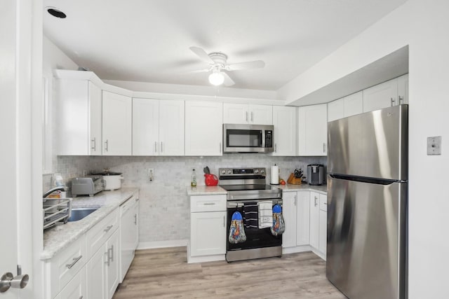 kitchen with white cabinets, stainless steel appliances, light hardwood / wood-style flooring, and light stone counters