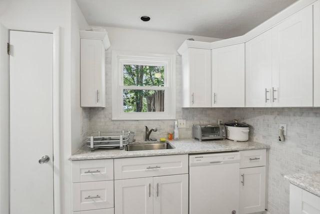 kitchen with light stone counters, dishwasher, backsplash, white cabinets, and sink