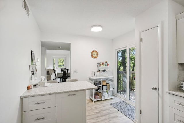 kitchen featuring white cabinets, a healthy amount of sunlight, light stone counters, and light wood-type flooring