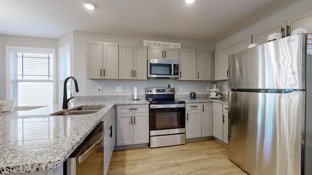 kitchen with stainless steel appliances, light hardwood / wood-style floors, sink, kitchen peninsula, and light stone counters