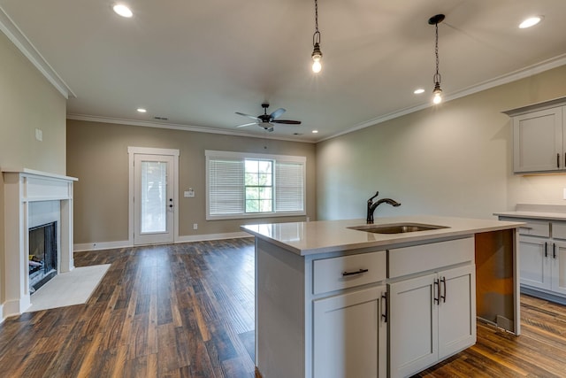 kitchen featuring sink, a center island with sink, a tiled fireplace, and ornamental molding