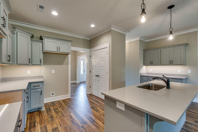 kitchen with an island with sink, crown molding, pendant lighting, dark wood-type flooring, and sink