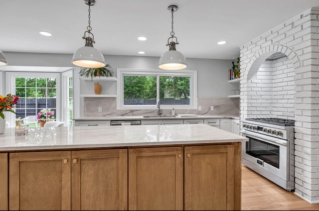 kitchen featuring sink, backsplash, light stone countertops, stainless steel range, and pendant lighting