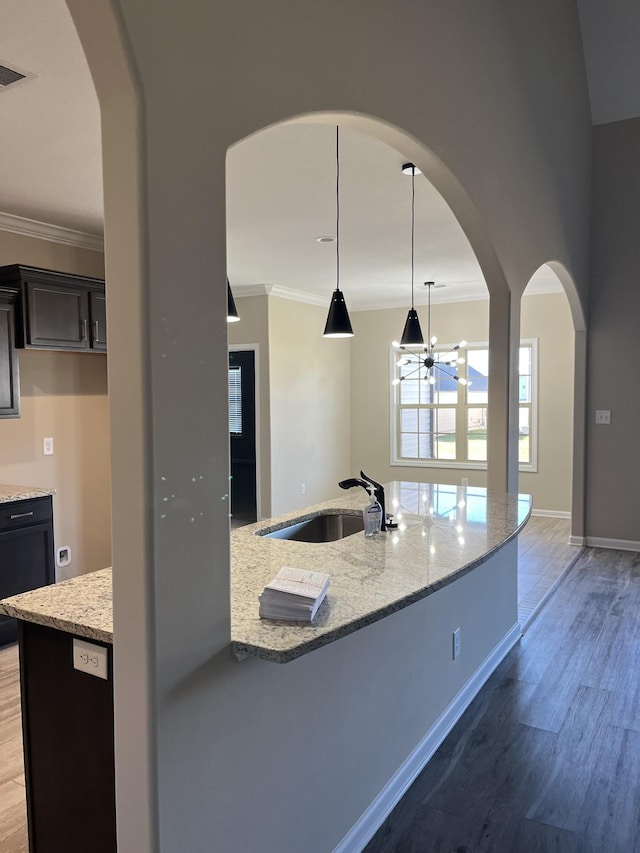 kitchen with hardwood / wood-style floors, an inviting chandelier, light stone counters, sink, and decorative light fixtures