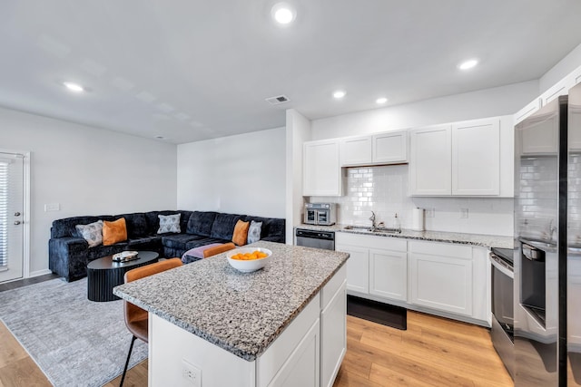 kitchen with light stone counters, a center island, white cabinetry, appliances with stainless steel finishes, and sink