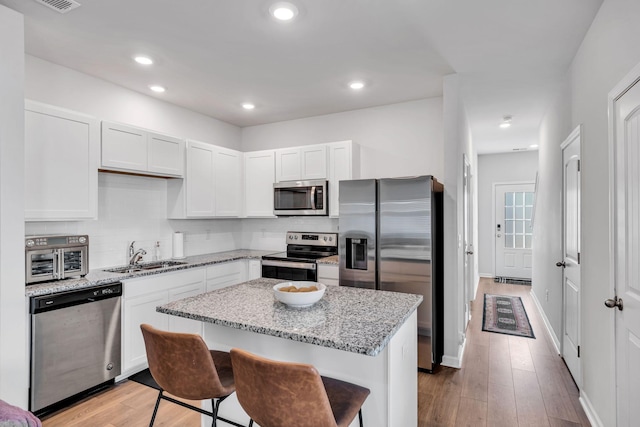 kitchen with a kitchen breakfast bar, appliances with stainless steel finishes, light stone counters, sink, and white cabinetry