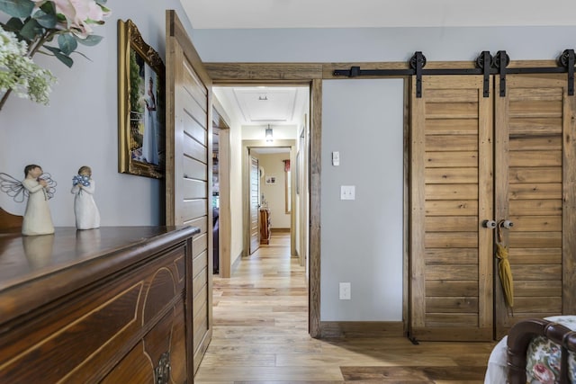 corridor with light wood-type flooring and a barn door