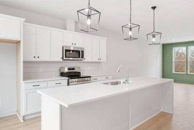 kitchen featuring a kitchen island with sink, stainless steel appliances, sink, white cabinetry, and decorative light fixtures