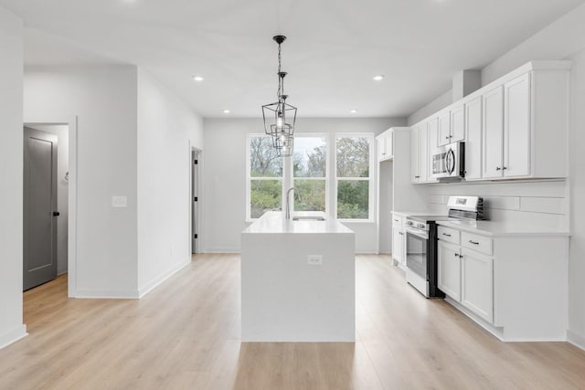 kitchen featuring pendant lighting, stainless steel appliances, an island with sink, white cabinetry, and sink