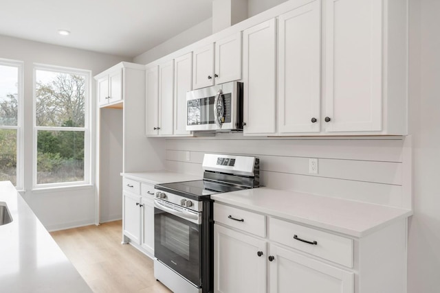 kitchen with stainless steel appliances, white cabinetry, a wealth of natural light, and light hardwood / wood-style flooring