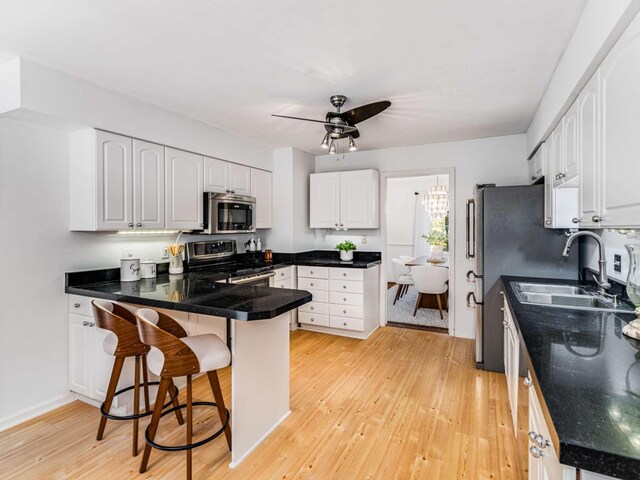 kitchen with a kitchen breakfast bar, stainless steel appliances, kitchen peninsula, sink, and white cabinetry