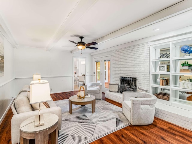 living room featuring wood-type flooring, ceiling fan, french doors, a fireplace, and beam ceiling