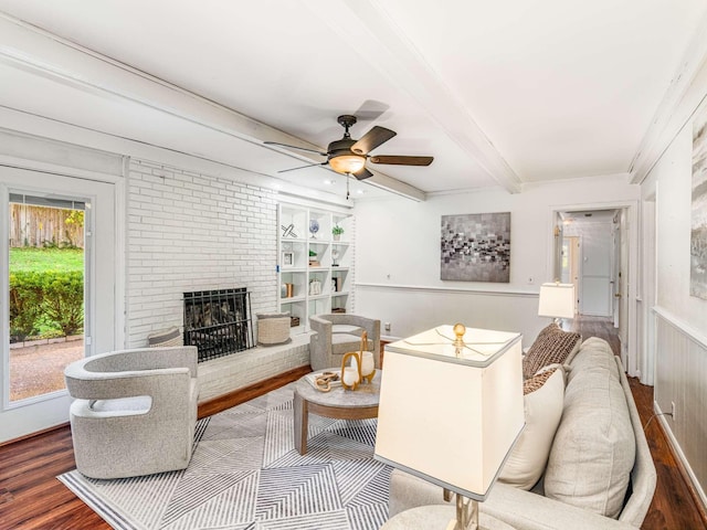 living room with hardwood / wood-style floors, ceiling fan, a brick fireplace, beam ceiling, and built in features