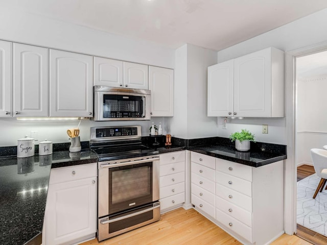 kitchen featuring appliances with stainless steel finishes, white cabinetry, dark stone counters, and light hardwood / wood-style floors