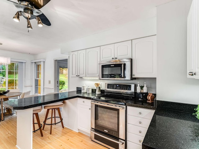 kitchen featuring kitchen peninsula, white cabinets, light wood-type flooring, and appliances with stainless steel finishes