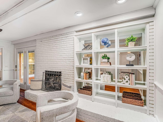 living area with a brick fireplace, light wood-type flooring, and ornamental molding