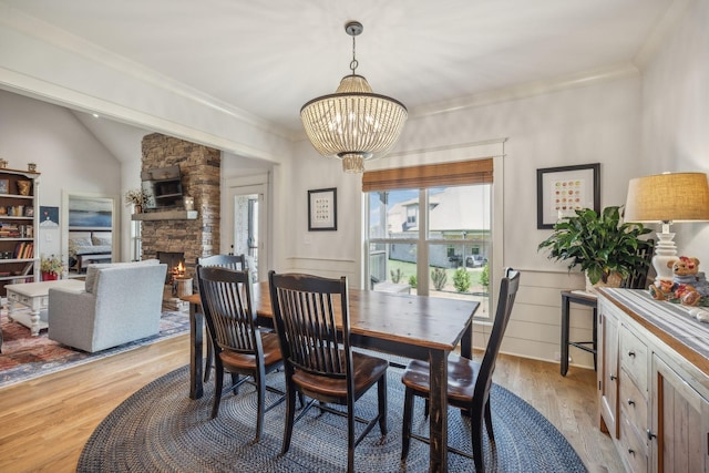 dining area with vaulted ceiling, light wood-type flooring, an inviting chandelier, crown molding, and a fireplace