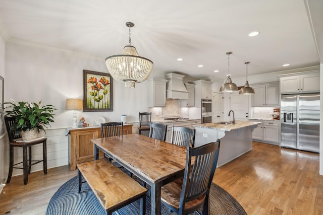 dining space featuring light wood-type flooring, ornamental molding, a chandelier, and sink