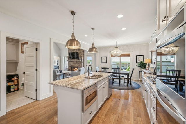 kitchen featuring stainless steel appliances, a kitchen island with sink, pendant lighting, and a stone fireplace