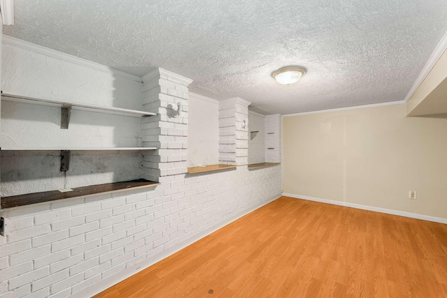 basement with hardwood / wood-style flooring, a textured ceiling, ornamental molding, and brick wall