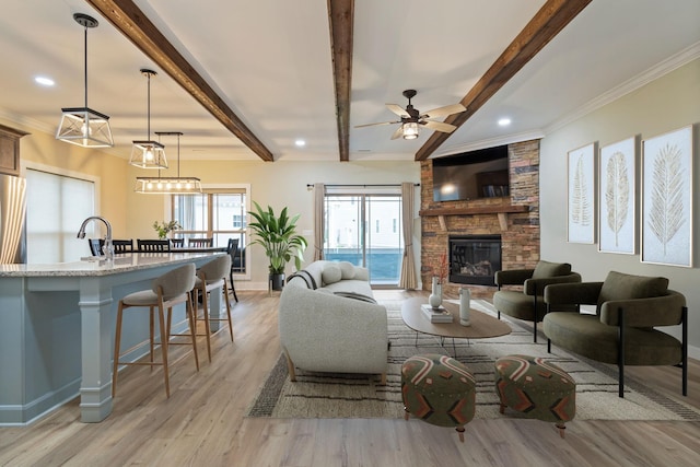 living room with light hardwood / wood-style flooring, beam ceiling, crown molding, ceiling fan, and a stone fireplace