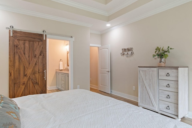 bedroom with light hardwood / wood-style flooring, a barn door, ensuite bath, a tray ceiling, and crown molding