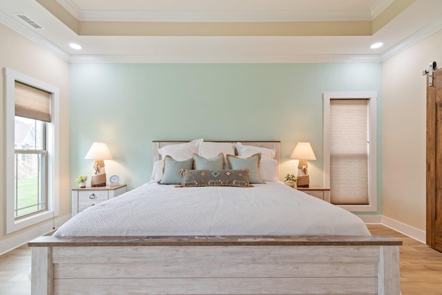 bedroom with light wood-type flooring, ornamental molding, a raised ceiling, and a barn door