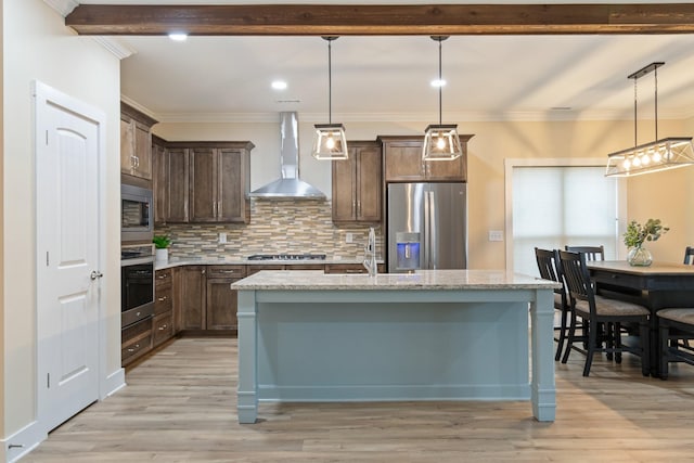 kitchen featuring appliances with stainless steel finishes, pendant lighting, a center island with sink, and wall chimney exhaust hood