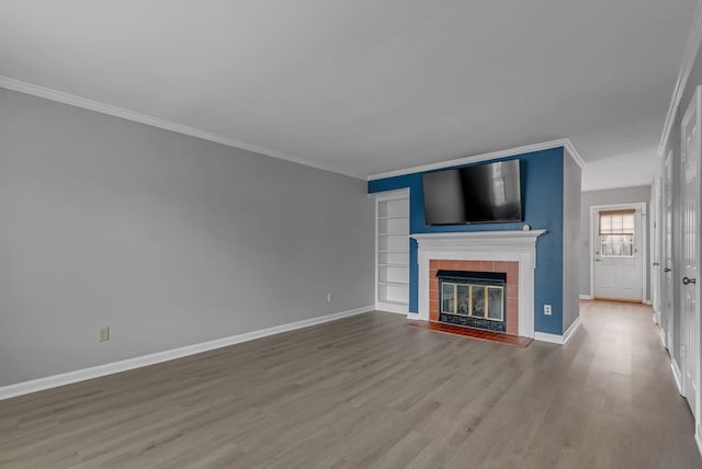 unfurnished living room with built in shelves, crown molding, a fireplace, and hardwood / wood-style floors