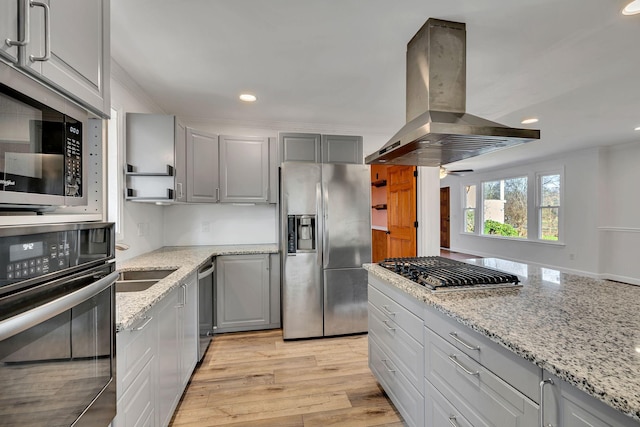 kitchen with island exhaust hood, gray cabinetry, stainless steel appliances, light stone countertops, and light hardwood / wood-style flooring