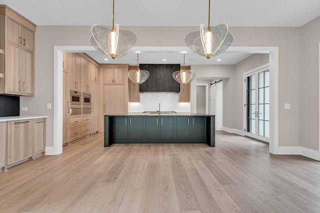 kitchen with light hardwood / wood-style flooring, light brown cabinetry, a barn door, hanging light fixtures, and exhaust hood