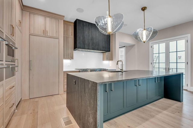 kitchen with a kitchen island with sink, light brown cabinetry, sink, light hardwood / wood-style flooring, and decorative light fixtures