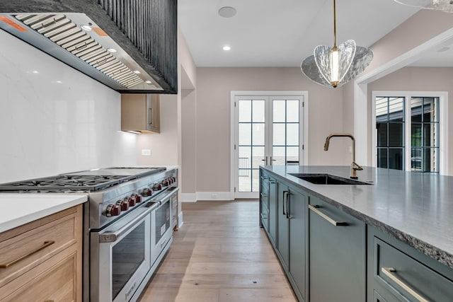 kitchen featuring decorative light fixtures, stainless steel appliances, wall chimney range hood, gray cabinets, and sink