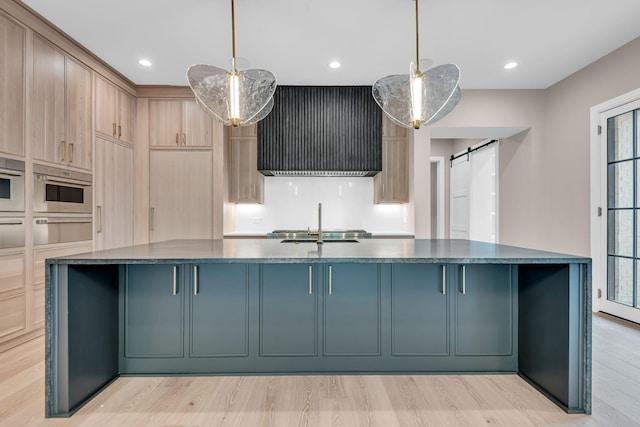 kitchen featuring wall chimney exhaust hood, light brown cabinetry, a barn door, and pendant lighting