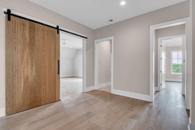 spare room featuring lofted ceiling, ceiling fan, a barn door, and light hardwood / wood-style flooring