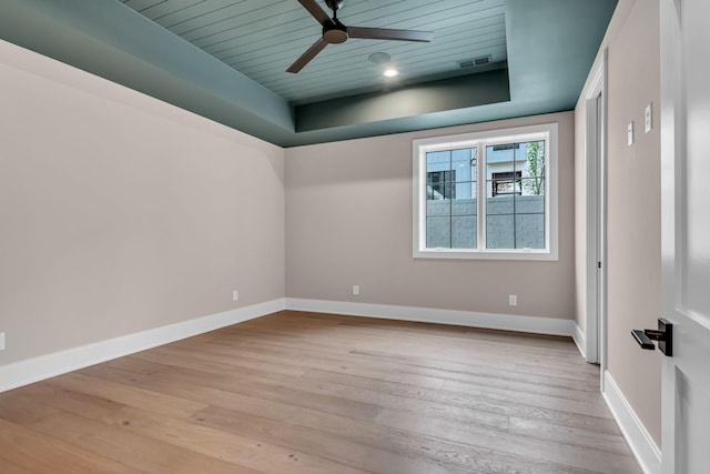 empty room featuring wooden ceiling, ceiling fan, a tray ceiling, and light hardwood / wood-style flooring