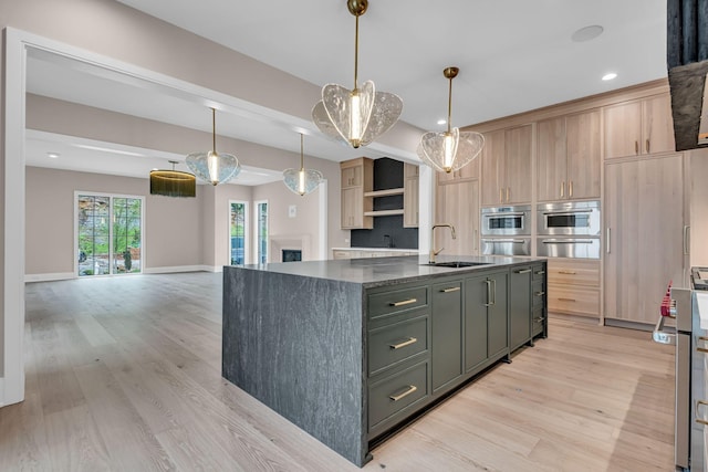 kitchen with light brown cabinetry, a center island with sink, pendant lighting, and sink