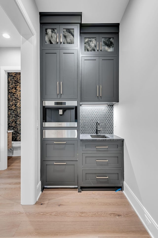 bar with sink, oven, light wood-type flooring, tasteful backsplash, and gray cabinets