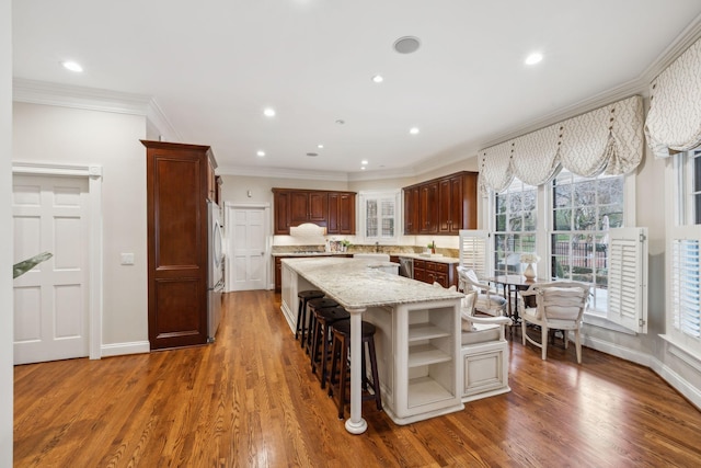 kitchen with dark wood-type flooring, stainless steel fridge, a kitchen bar, a kitchen island, and crown molding