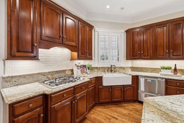 kitchen with light stone counters, light wood-type flooring, appliances with stainless steel finishes, and sink