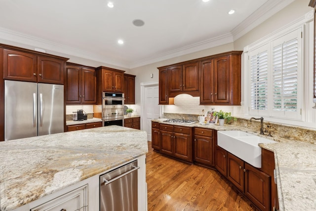 kitchen with sink, light stone counters, ornamental molding, tasteful backsplash, and appliances with stainless steel finishes